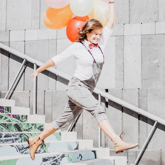 Nancy springt mit Luftballons in der Hand über Stiegen